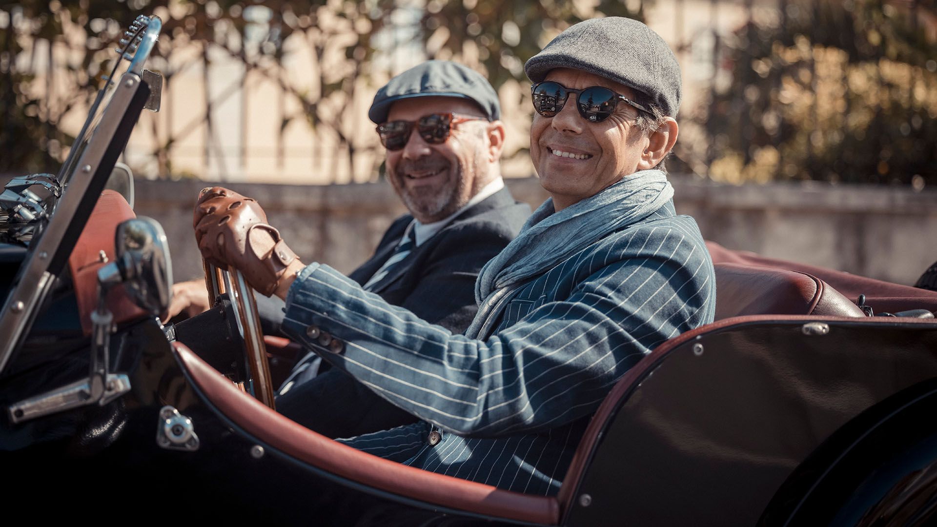 Photo of two very dapper-looking gentleman, participating in the Distinguished Gentleman's Ride, smiling to camera from a classic car.