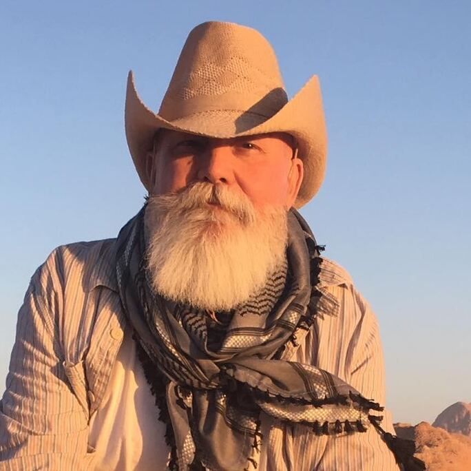Cowboy hat-wearing man, sporting an outstanding grey beard and moustache, looking to camera.