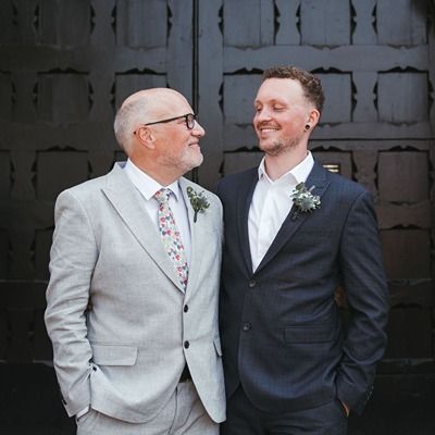 Photo of a young man in a wedding suit beaming proudly next to his father.