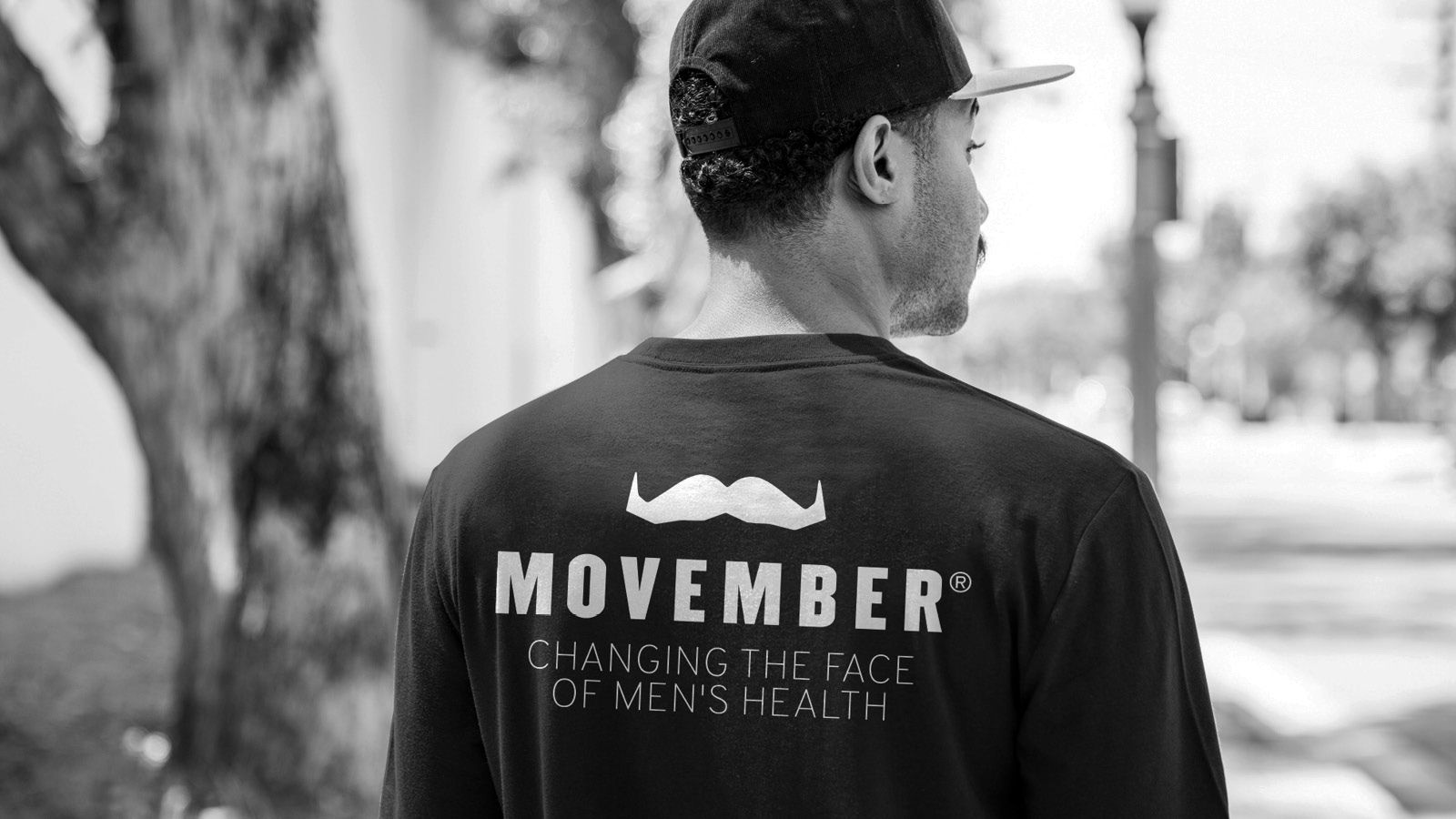 Black and white photo showing the back of a man wearing a stylish Movember-branded shirt.