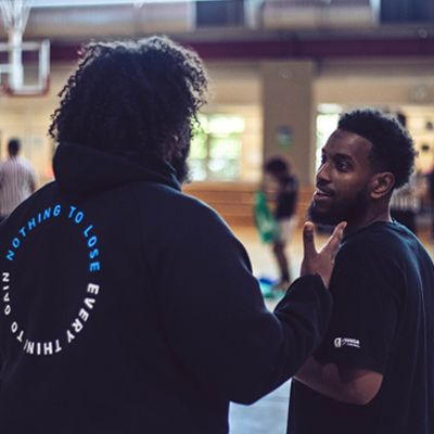 Photo of two young men conversing at a basketball court.